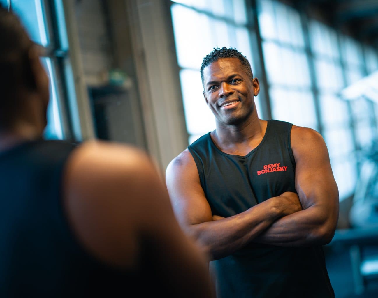 Remy Bonjasky standing with his arms crossed, talking to someone in the gym.