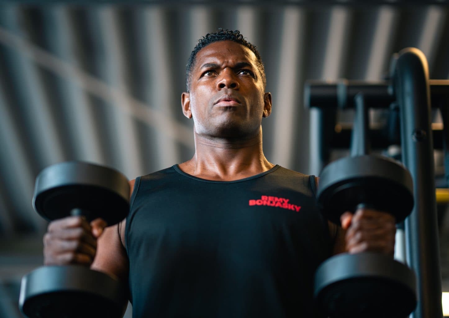 Remy Bonjasky training with dumbbells in the gym, looking up, focused.